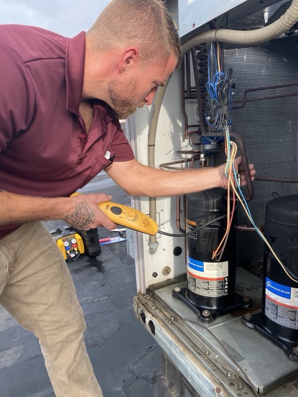 Technician diagnosing a rooftop condenser's compressor and wiring