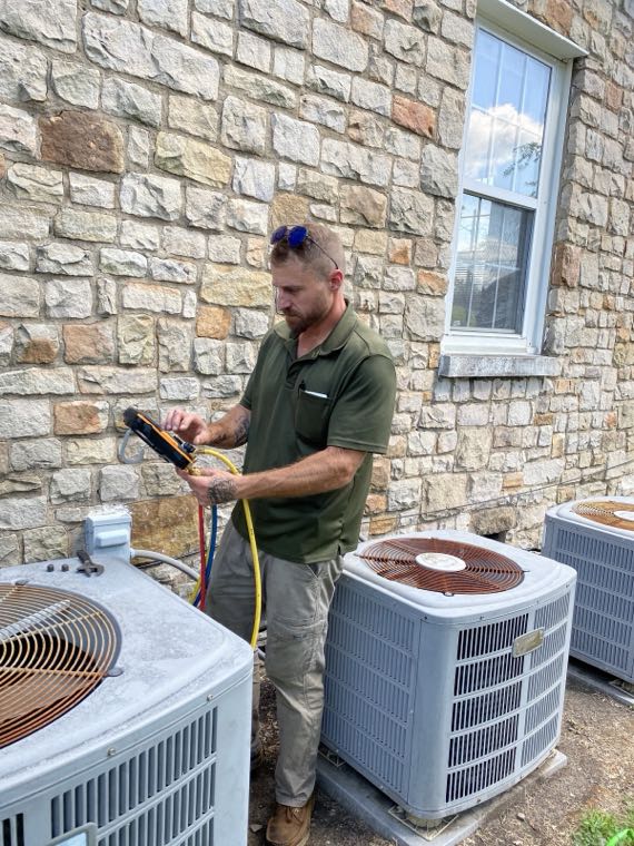 H & H technician checking gauges beside two condensers at a stone home