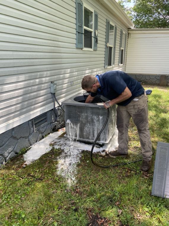 Technician cleaning an outdoor condenser coil with foam cleaner